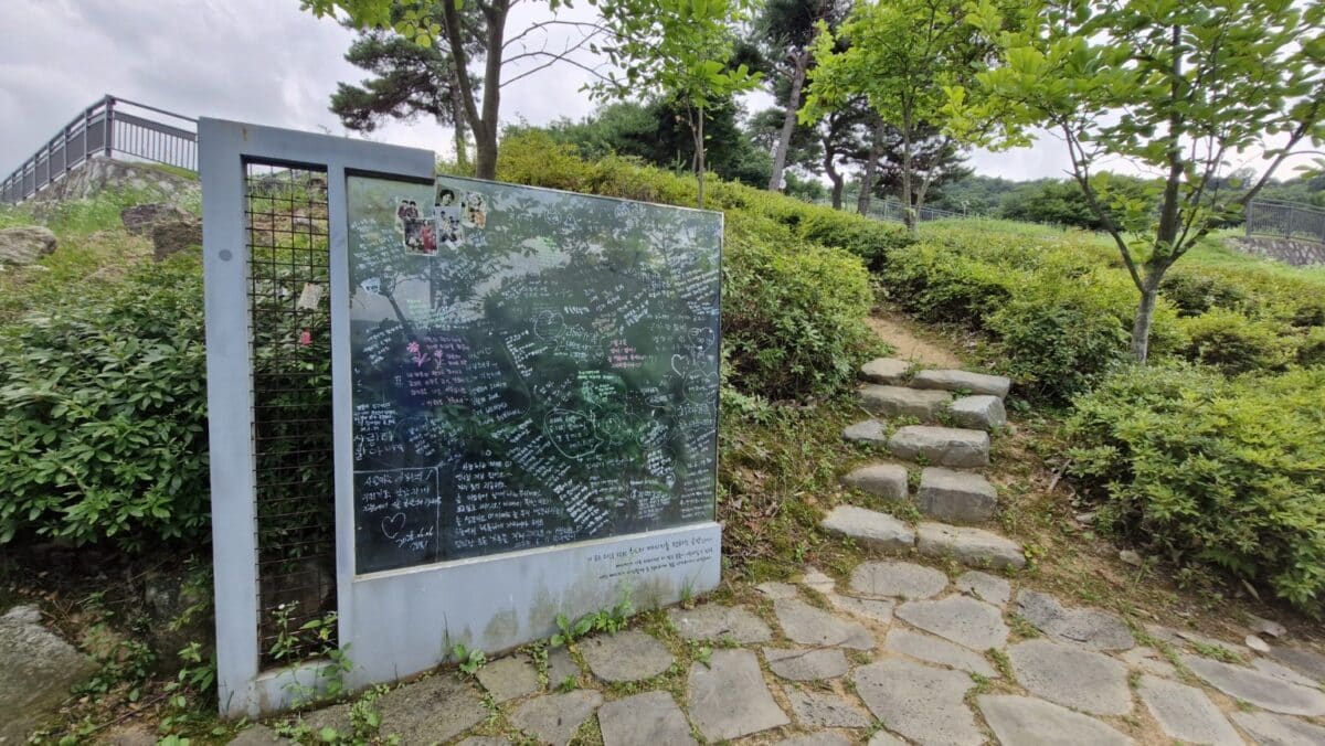 고인을 향한 손글씨 메시지로 가득한 유리 추모벽과 돌계단이 이어진 산길